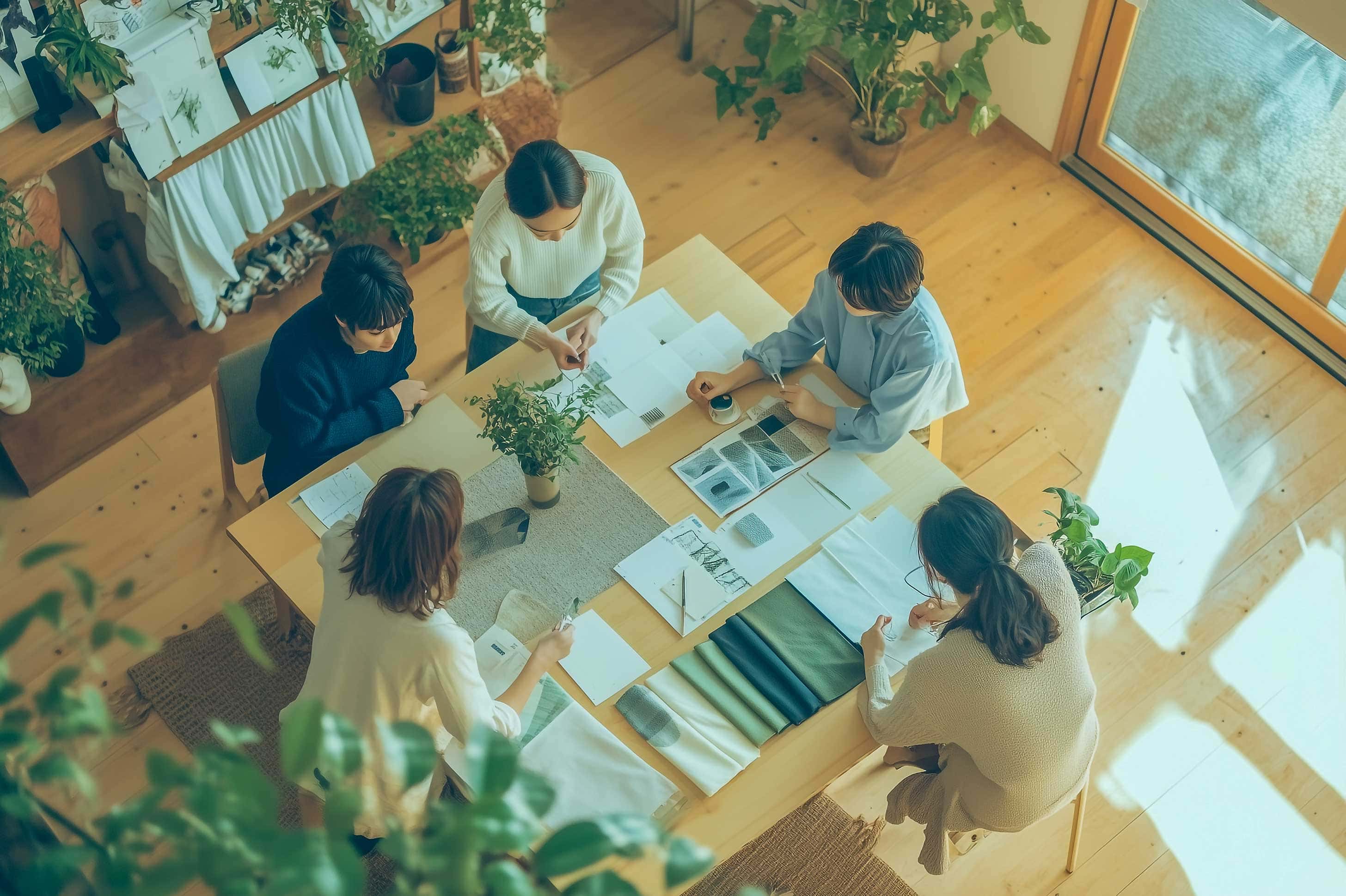 テーブルを囲み、資料や布のサンプルを広げて打ち合わせしている５人の上からの眺め